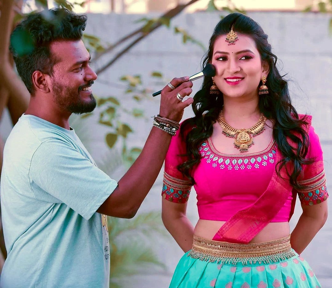 Aarav applying blush with a brush to a model in a pink blouse and turquoise half-saree during an outdoor shoot