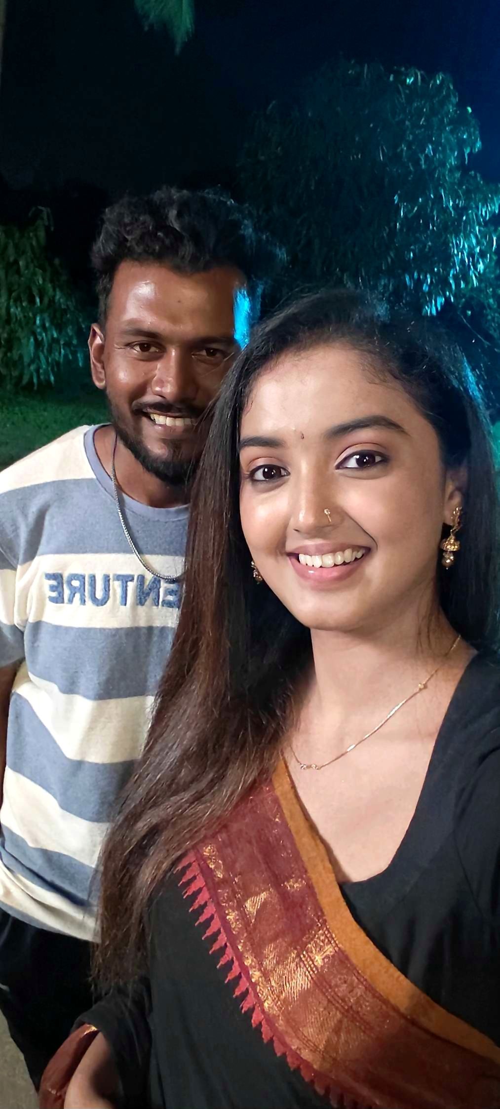 Aarav on location in the evening with a client in a black saree with a red zari border